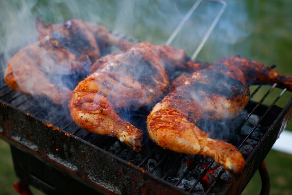 Close-up of spicy chicken grilling on a charcoal barbecue with visible smoke outdoors.